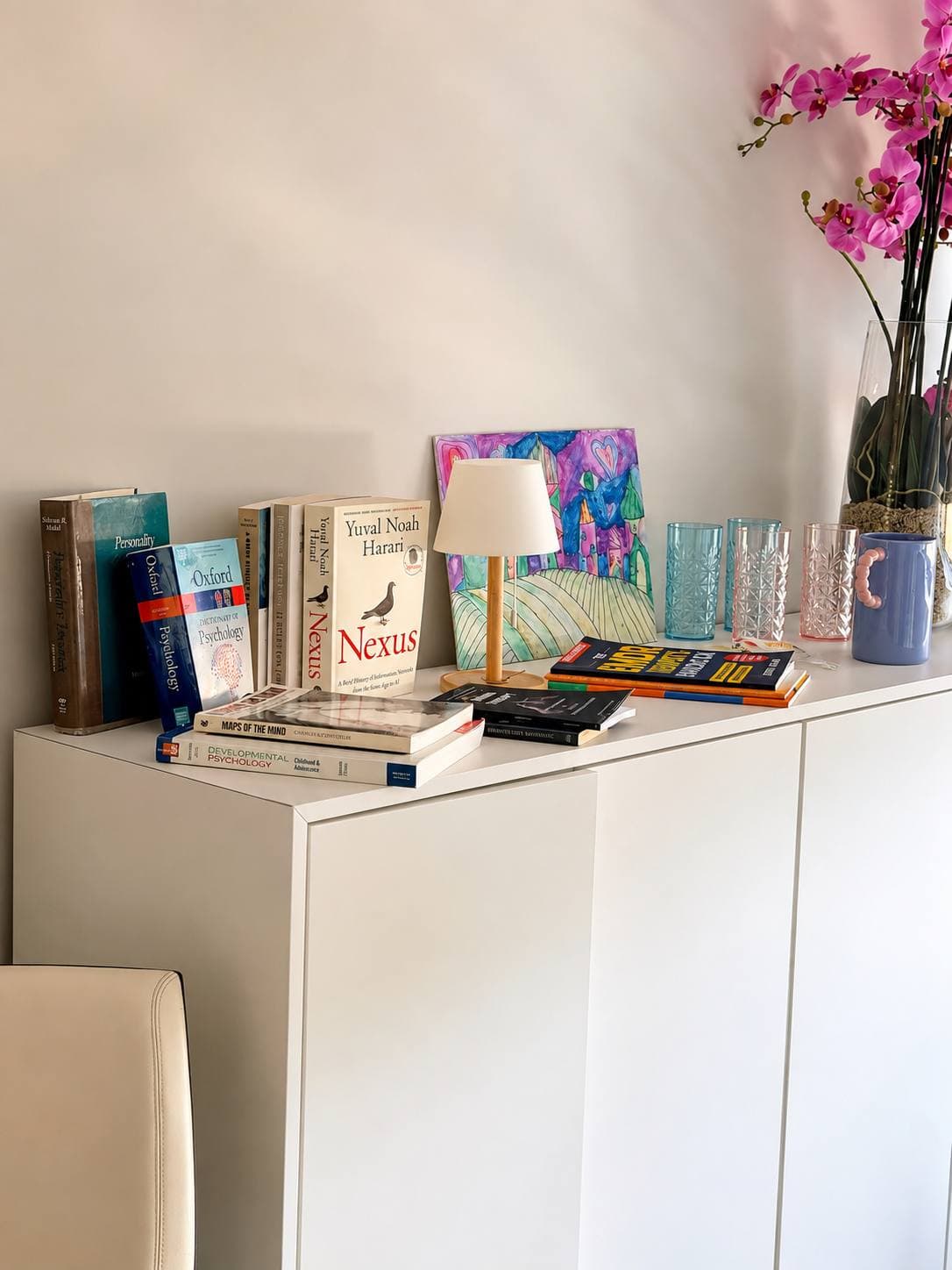 Полка с книгами по психологии, настольная лампа и орхидея